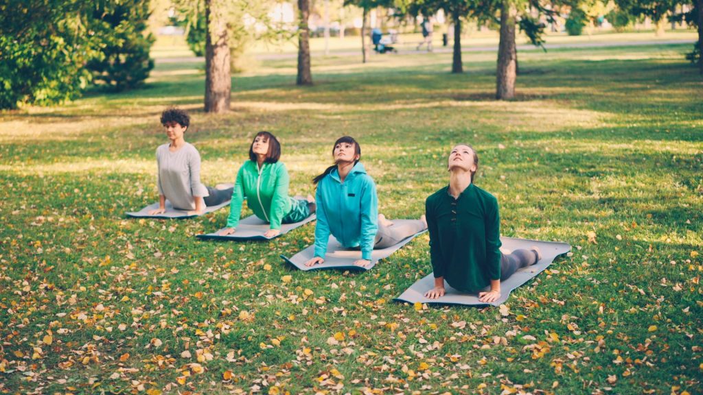 Quatre personnes pratiquent le yoga sur des tapis dans un parc.