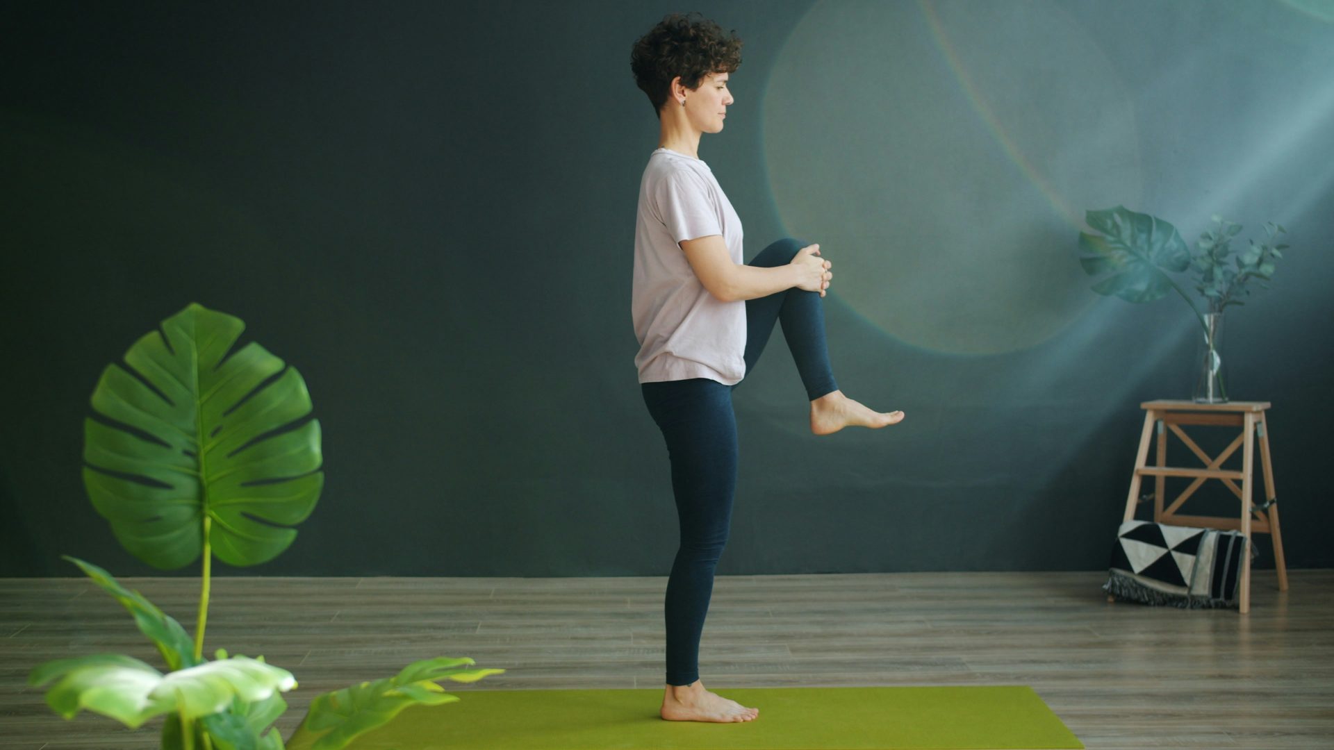 Une femme pratique le yoga sur un tapis vert à l'intérieur.