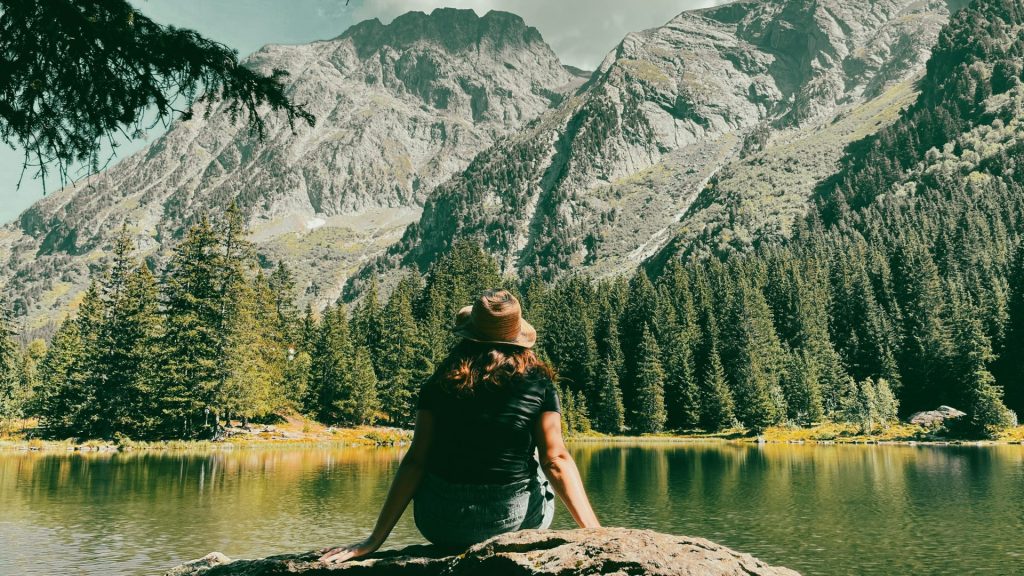 a woman sitting on a rock in front of a mountain lake